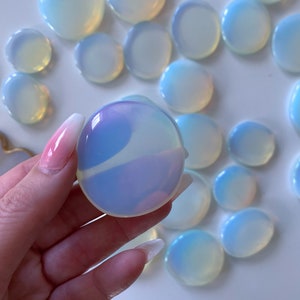 May include: A collection of iridescent opalite stones in various sizes and shapes. The stones are smooth and polished, with a milky white color and a hint of blue.