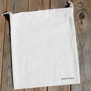 May include: A white cotton drawstring bag with the text "MakerTheory" printed in black on the bottom.