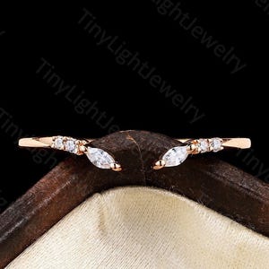 May include: A rose gold open ring featuring two marquise-cut stones and four small round-cut stones arranged symmetrically on each side of the band. The ring has a curved, V-shaped design that tapers toward the center, creating an open gap.