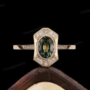 May include: A gold ring with a green oval gemstone surrounded by smaller diamonds. The ring has a geometric design with a pointed top and bottom.