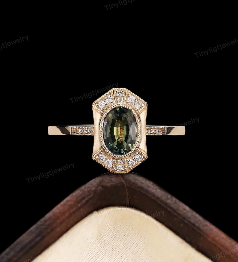 May include: A gold ring with a green oval gemstone surrounded by smaller diamonds. The ring has a geometric design with a pointed top and bottom.