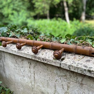 Puede incluir: Un perchero de madera vintage con cinco clavijas torneadas. El perchero es de color marrón cálido y tiene un diseño similar al bambú. Las clavijas están espaciadas uniformemente a lo largo del perchero.