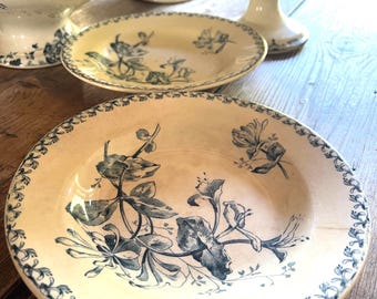 May include: A collection of antique cream-coloured ceramic tableware with blue floral designs. The set includes plates, a serving bowl, and a tiered serving stand, all featuring intricate patterns and a vintage aesthetic. The plates have a diameter of approximately 25 cm.