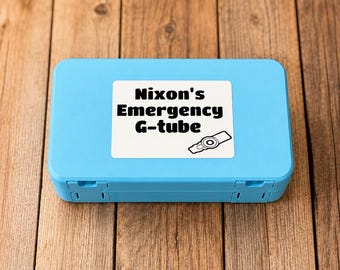 May include: A rectangular light blue plastic storage case featuring a white label on the lid. The label displays the black text Nixon's Emergency G-tube and a small black and white graphic illustration of a medical feeding tube device.