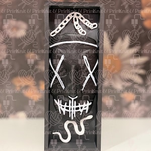 May include: A black mask with white accents in a rectangular frame. The mask features white X-shaped eyes, a stitched mouth, and a chain-like design above. The frame is dark gray, and the background has a repeating pattern.