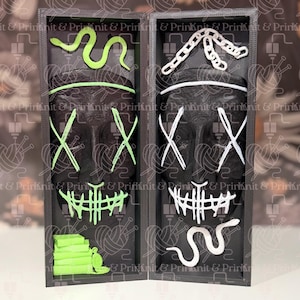 May include: Two black skull masks with white and neon green accents, displayed in a black box. The masks have an X-shaped design over the eyes and a stitched mouth. The box contains a neon green snake and other decorative elements.