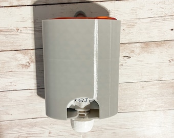 May include: A gray plastic dispenser with a white pump and a clear orange top. The dispenser is mounted on a white wooden wall.