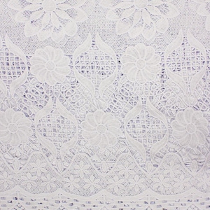May include: Close-up of white lace fabric with a floral pattern. The lace features detailed floral and geometric designs, creating a delicate and intricate texture. The pattern includes large flowers and smaller, repeating motifs.