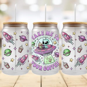 May include: Clear glass tumbler with a bamboo lid and a white straw. The tumbler features a colorful design with an alien in a spaceship, rockets, planets, stars, and the text "Take Me To Your Coffee."