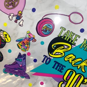Peut inclure: Ensemble d'autocollants sur le th&egrave;me des ann&eacute;es 90, avec un Polly Pocket rose, un yo-yo, un ours Beanie Baby color&eacute; et des rollers violets. La phrase &laquo;&nbsp;Take Me Back To The 90s&nbsp;&raquo; est &eacute;galement pr&eacute;sente.
