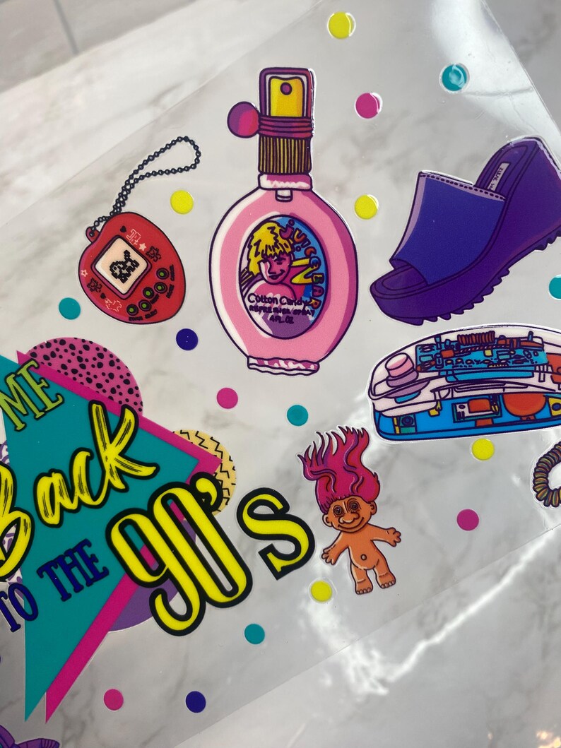 Peut inclure: Ensemble d'autocollants sur le th&egrave;me des ann&eacute;es 90. Comprend un flacon de parfum rose, un jeu portable rouge, une sandale &agrave; plateforme violette, un t&eacute;l&eacute;phone bleu et une poup&eacute;e troll. La phrase "Welcome Back to the 90's" est &eacute;galement pr&eacute;sente.