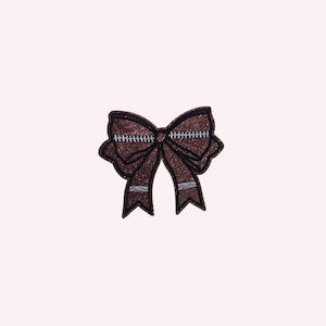 May include: A brown glitter bow with black and silver detailing. The bow features a stitched design in the centre and on the edges. This is a decorative item.