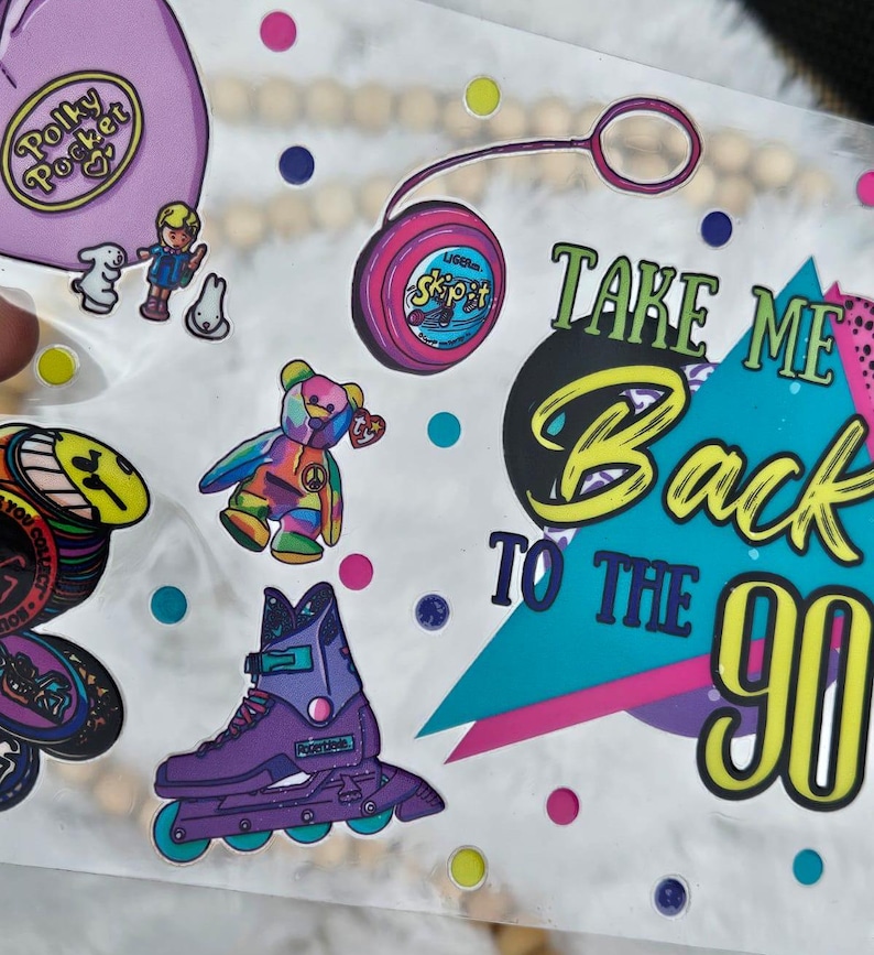 Peut inclure: Une collection d'autocollants color&eacute;s sur le th&egrave;me des ann&eacute;es 90. Comprend un sac Polly Pocket, un yo-yo, un ours en peluche arc-en-ciel, un patin &agrave; roulettes violet et l'expression "Take Me Back To The 90s."