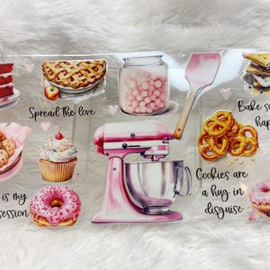 May include: A collection of watercolor illustrations featuring baked goods and baking tools. Includes a red velvet cake, apple pie, cookies, cupcake, donut, pretzels, brownies, and a pink stand mixer. Text includes "Spread the love" and "Bake someone happy."