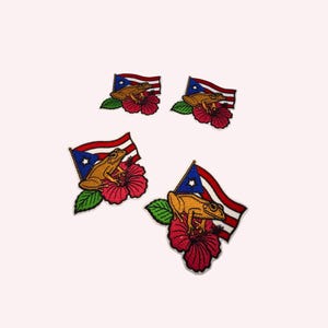 May include: Four embroidered patches featuring a golden coqui frog perched on a red hibiscus flower with a Puerto Rican flag in the background. The design includes a green leaf, a blue triangle with a white star, and red and white stripes.