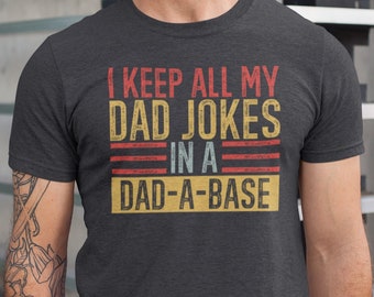 May include: A dark heather grey t-shirt with a vintage-style graphic that reads "I keep all my dad jokes in a dad-a-base".