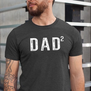 May include: A dark heather grey t-shirt with the text "DAD²" printed in white on the front.
