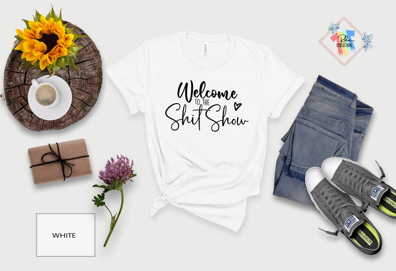 May include: White t-shirt with the text "Welcome to the Shit Show" in black cursive lettering with a small heart symbol.