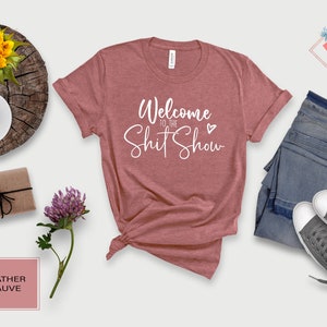 May include: Heather mauve t-shirt with the text "Welcome to the Shit Show" in white cursive lettering with a small white heart.