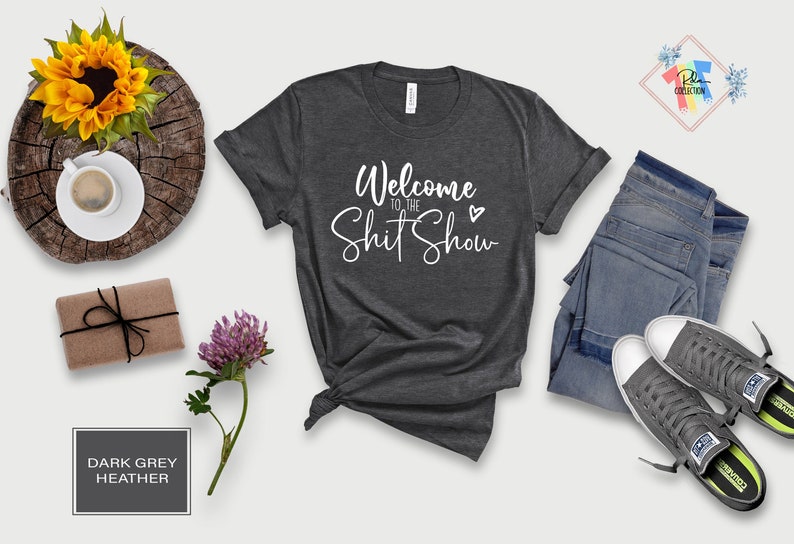 May include: Dark grey heather t-shirt with the text "Welcome to the Shit Show" in white cursive lettering with a small heart.