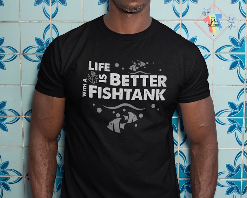 Puede incluir: Camiseta negra con el texto blanco "LIFE IS BETTER WITH A FISHTANK". El dise&ntilde;o incluye ilustraciones de peces, burbujas y olas. La camiseta es de cuello redondo y tiene mangas cortas.
