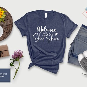 May include: A heather navy blue t-shirt with the text "Welcome to the Shit Show" in white cursive lettering with a small heart.