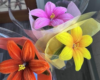 May include: A bouquet of three artificial flowers wrapped in clear plastic and yellow tissue paper. The flowers are orange, pink, and yellow.