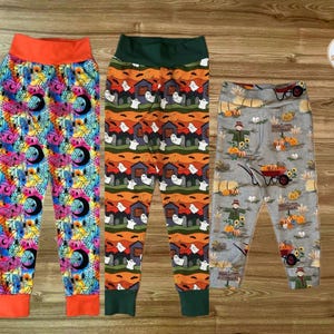 May include: Three pairs of patterned leggings. One pair has a colourful floral and moon design with orange trim. Another has a Halloween-themed pattern with ghosts and houses. The third pair features scarecrows and pumpkins.
