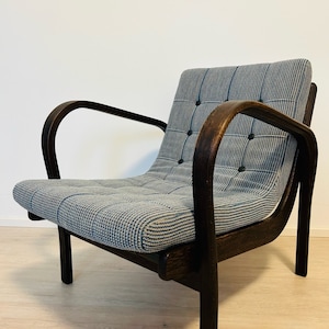 Op de afbeelding: Een donkerhouten fauteuil met een grijze en witte geruite stoffen bekleding. De stoel heeft gebogen armleuningen en een knoopgestoffeerde rugleuning.