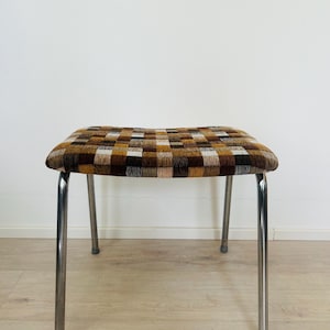 May include: A stool with four slender, polished chrome metal legs and a rectangular seat upholstered in a textured fabric featuring a multi-coloured, woven checkerboard pattern in shades of brown, tan, black, white, and grey.