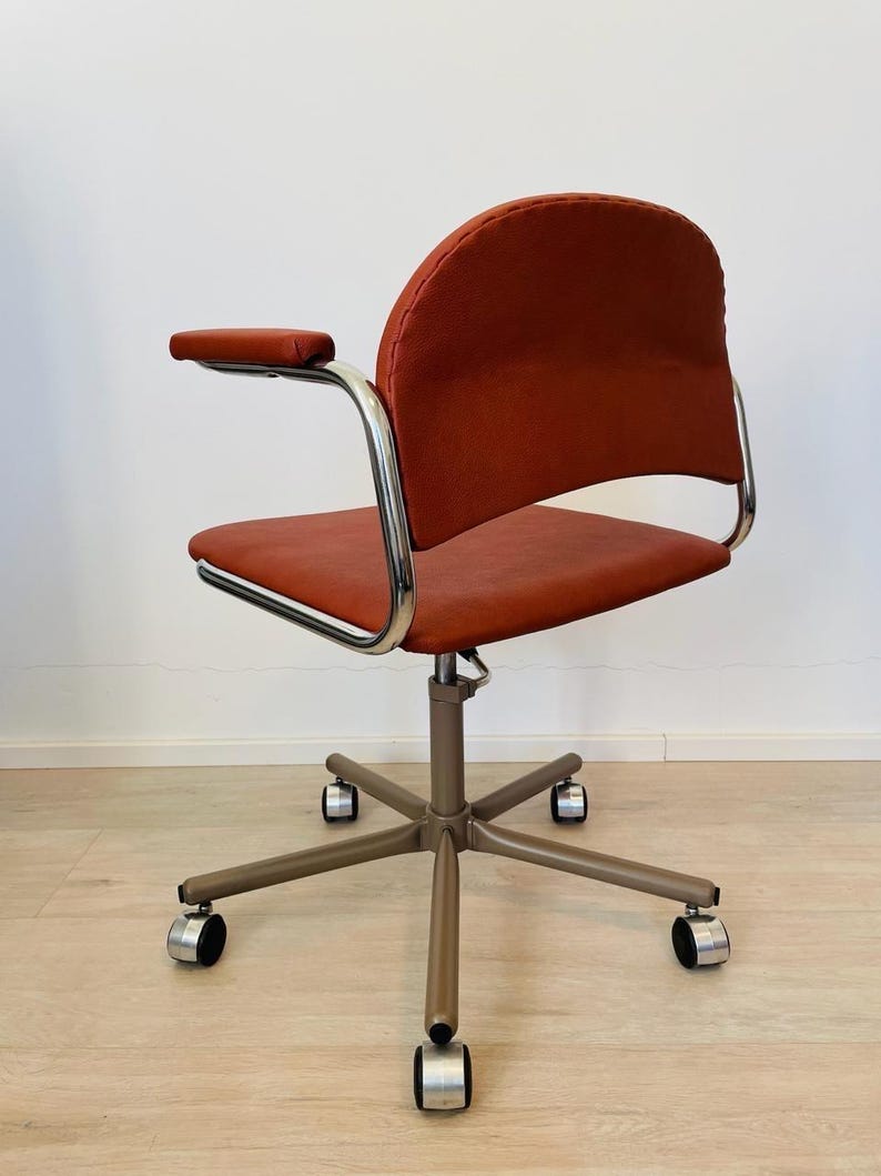 May include: A red office chair with chrome arms and a swivel base with five wheels. The chair has a padded seat and back.