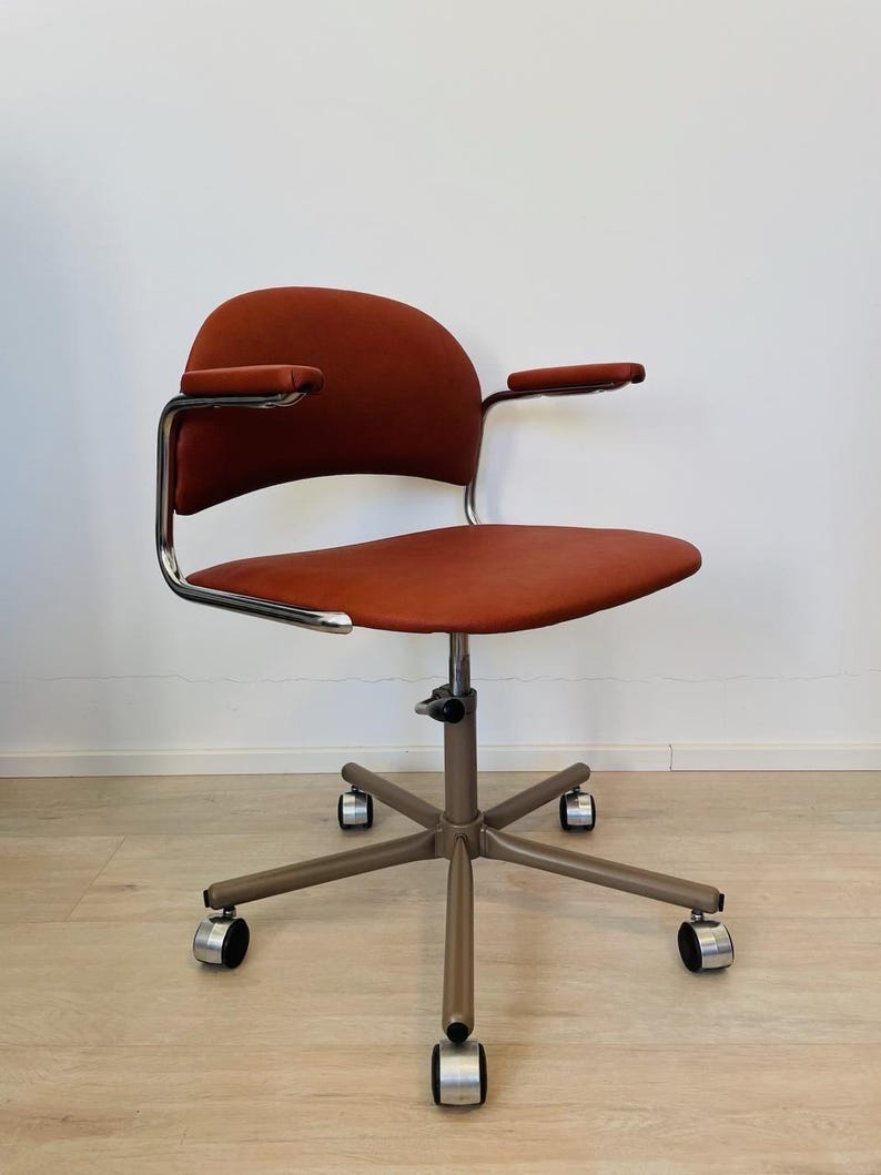 May include: A red office chair with chrome arms and a swivel base with five wheels. The chair has a padded seat and back.