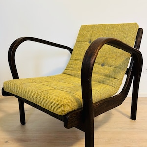 Op de afbeelding: Een gele fauteuil met donkerbruine houten armleuningen en poten. De stoel heeft een gestoffeerde zitting en rugleuning.