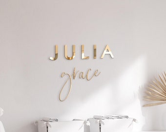 Op de afbeelding: Een witte commode met vier lades en zilveren handgrepen. Een witte commode met een witte commodemat en een beige deken met pompoenen staat op de commode. Een wit konijnenbeeldje staat op een plank boven de commode. De muur achter de commode heeft gouden letters die "JULIA grace" spellen.