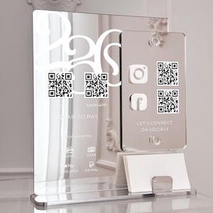 May include: A clear acrylic sign with a mirrored finish. The sign has QR codes, the text "SCAN TO PAY", and social media icons. It also includes payment options like Apple Pay and PayPal. A small card holder is at the base.