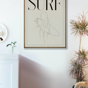 May include: A minimalist line art print of a person holding a surfboard with the word "SURF" in black text above the image.