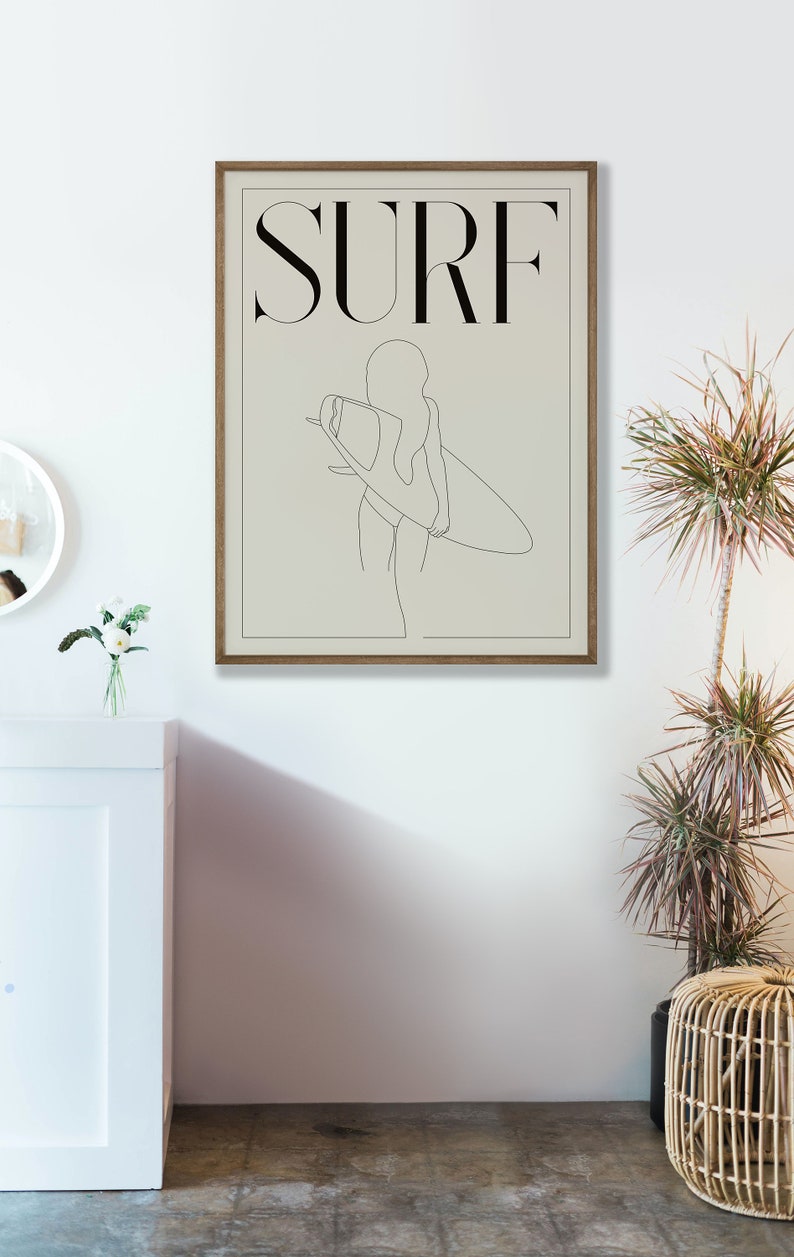 May include: A minimalist line art print of a person holding a surfboard with the word "SURF" in black text above the image.