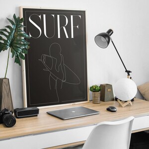 May include: A black and white line art print of a woman holding a surfboard with the word "SURF" in white text on a black background.