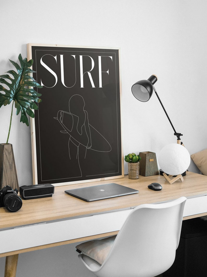 May include: A black and white line art print of a woman holding a surfboard with the word "SURF" in white text on a black background.