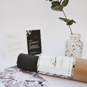 May include: A rolled up poster with a white label that says "French Pair" and "Affiches et Images d'Art". The poster is sitting on a white surface with a black and white card and a small vase with a green plant.