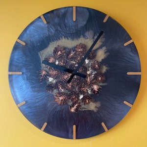 May include: A black and gold clock with a resin face featuring a design of dried flowers. The clock has gold-colored hands and a black frame.