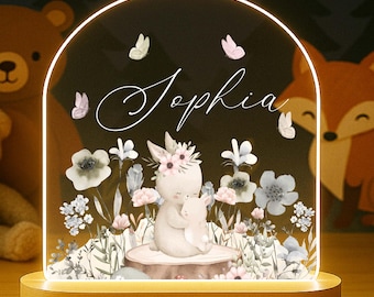 May include: A night light with a wooden base and a clear acrylic arch. The arch features a floral design with a bunny and the name "Sophia". A teddy bear and a fox are in the background.