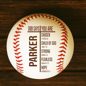 May include: A white baseball with red stitching and the text "GOD SAYS YOU ARE" and "PARKER". Additional text includes "CHOSEN", "CHILD OF GOD", "STRONG", "FEARLESS", and "HOPE", with associated Bible verses.