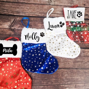 May include: Four personalized Christmas stockings with white felt and a variety of colors and patterns. The stockings are decorated with stars and paw prints. The names "Mila", "Molly", "Luna", and "Jake" are written on the stockings.