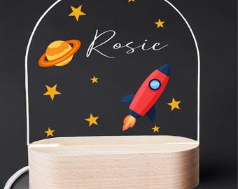 May include: A wooden night light with a clear acrylic panel featuring a rocket, a planet, stars, and the name "Rosie".