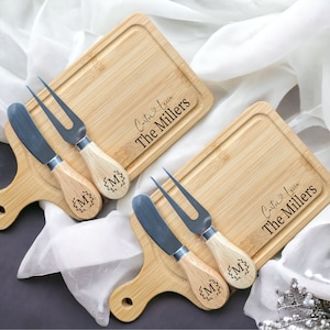 May include: Two wooden cheese boards with handles, each with a knife and a fork. The boards are engraved with the text "Cait & Kevin The Millers".