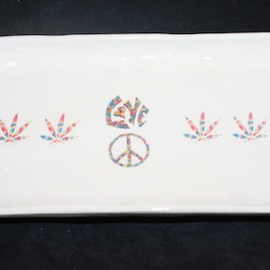 May include: White ceramic rolling tray with a peace sign and the word "LOVE" in colorful, patterned letters. The tray also features four marijuana leaf designs.