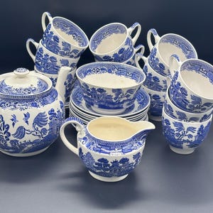 May include: A complete blue and white porcelain tea set. The set includes a teapot, creamer, cups, saucers, and bowls. The design features a classic willow pattern. The tea set is arranged on a dark surface.
