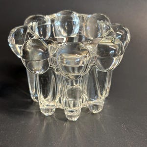 Op de afbeelding: Een heldere glazen kaarsenhouder met een uniek ontwerp met een reeks ronde bulten rond de boven- en onderkant. De houder heeft een getextureerd, geribbeld ontwerp.