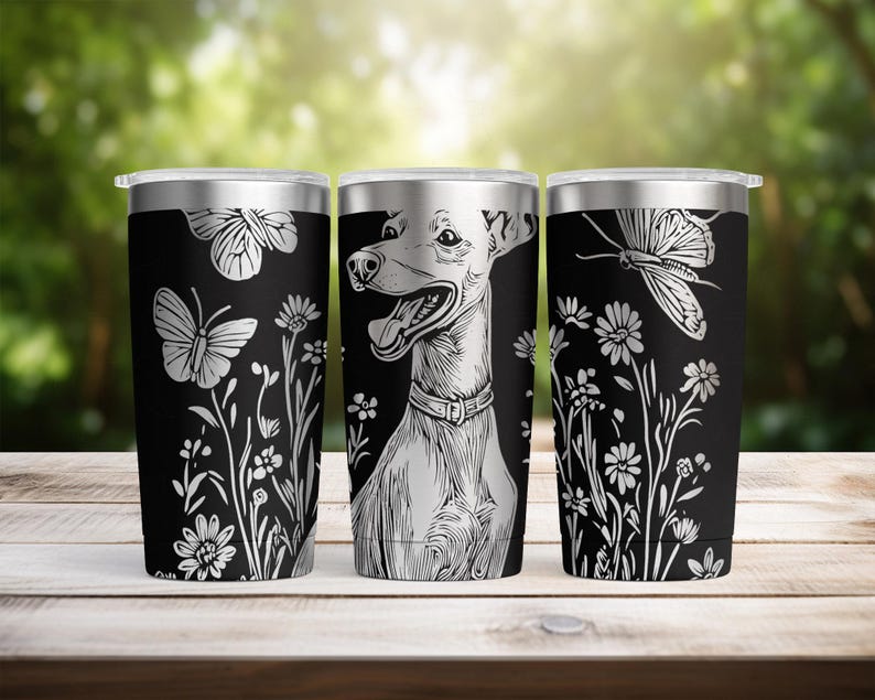 May include: Three black stainless steel travel mugs with silver lids. Each mug has a white illustration: one with butterflies and flowers, one with a dog, and one with a butterfly and flowers. The mugs are on a wooden surface.